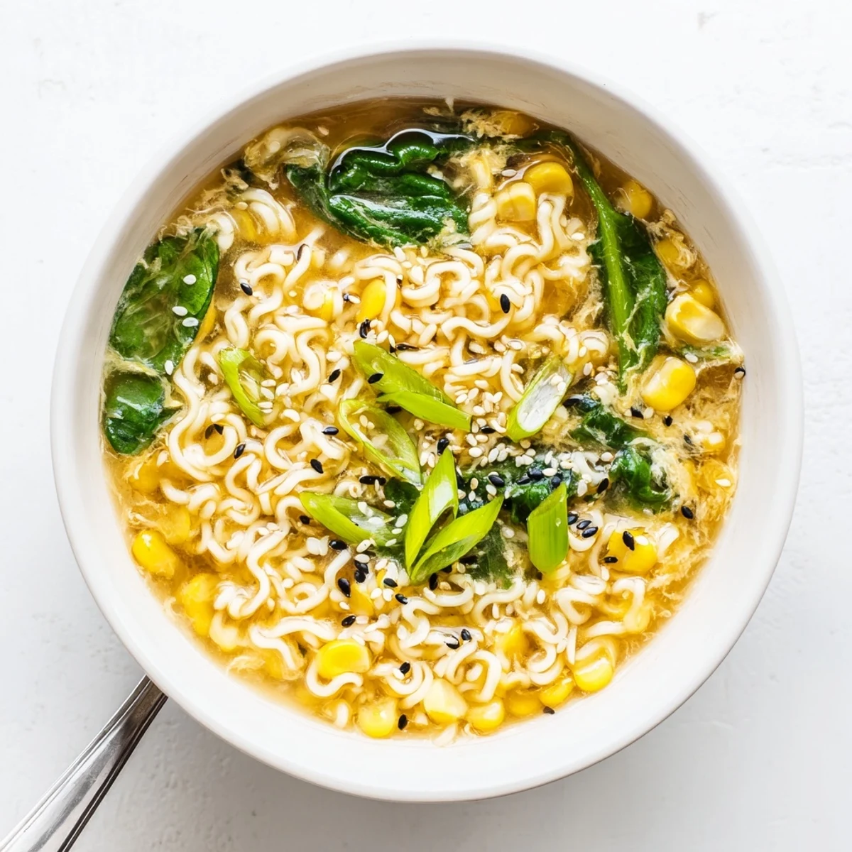 A steaming bowl of Elevated Ramen Egg Drop Soup garnished with fresh scallions and toasted sesame seeds.