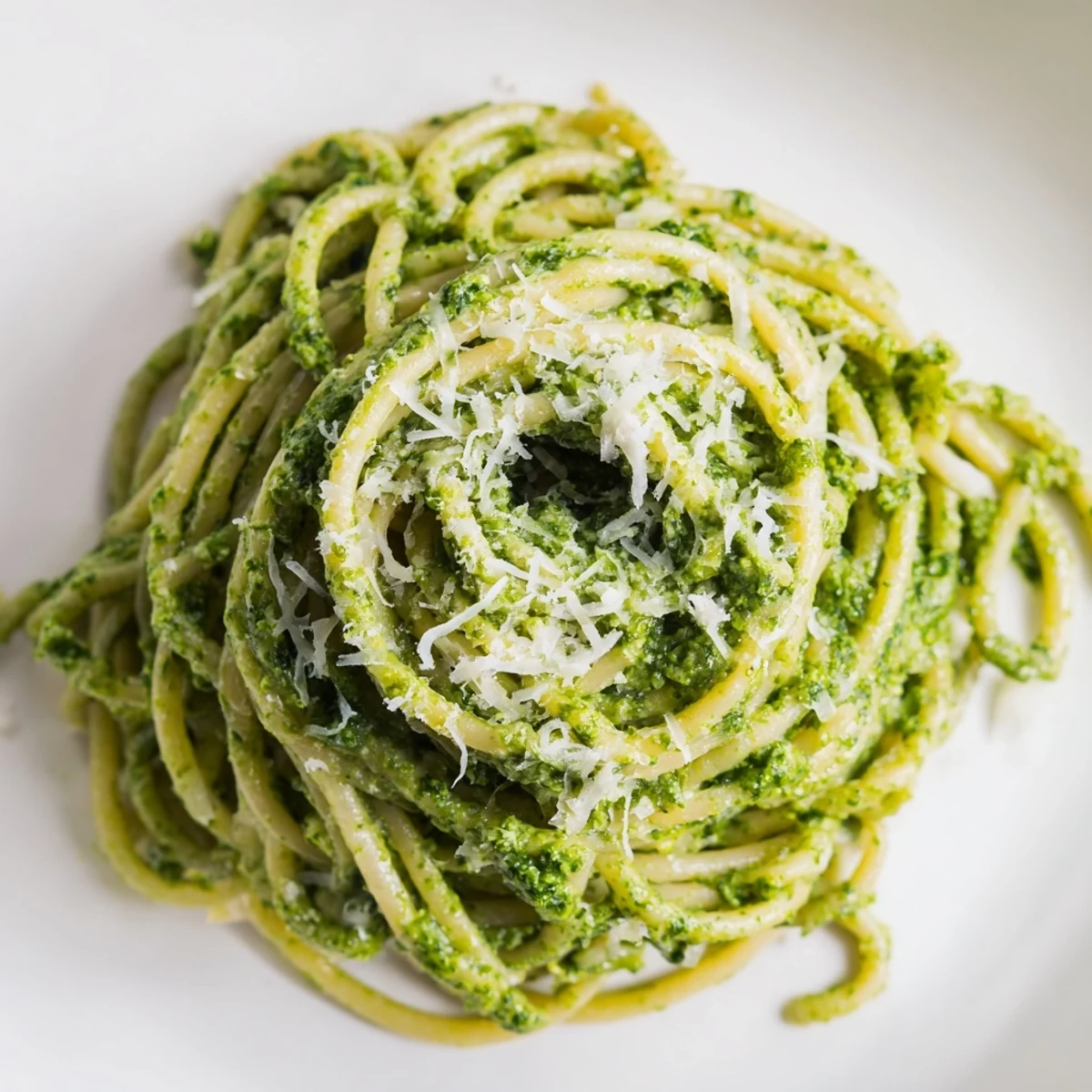 Creamy Sunflower Seed Pesto Pasta twirled onto a plate, topped with fresh basil leaves and a generous shower of Parmesan cheese.