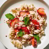 A beautiful bowl of sweet strawberry yogurt pasta is garnished with fresh mint and almonds.