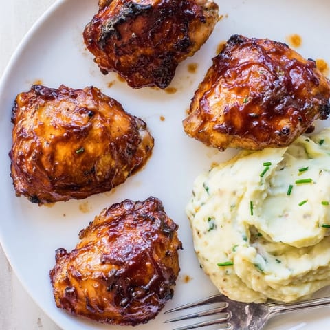 Golden-brown honey BBQ chicken thighs drizzled with sauce, alongside fluffy garlic mashed potatoes.  