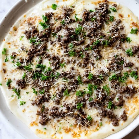 This Ground Beef Alfredo Pizza shows a bubbly, golden crust with creamy Alfredo and hearty beef.