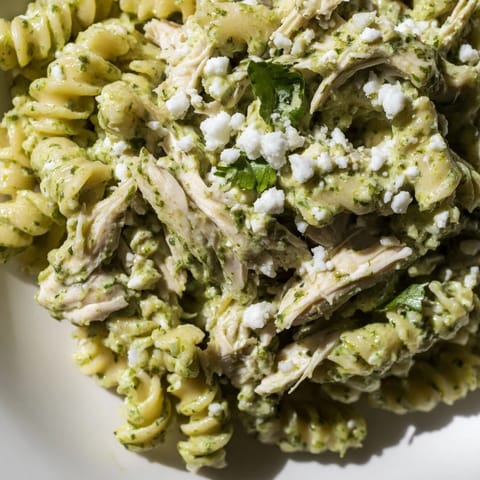 A vibrant serving of Cilantro Lime Chicken Pasta on a rustic plate, featuring bright green sauce, crumbled cotija cheese, and lime zest.  