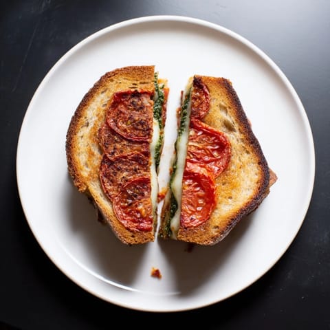 A close-up of the Roasted Tomato Pesto Grilled Cheese shows caramelized tomatoes and vibrant green pesto.