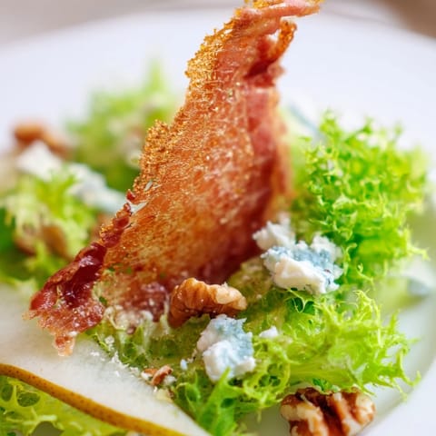 A fork-ready image of Frisée, Pear, Blue Cheese, and Crispy Prosciutto Salad drizzled with tangy vinaigrette.