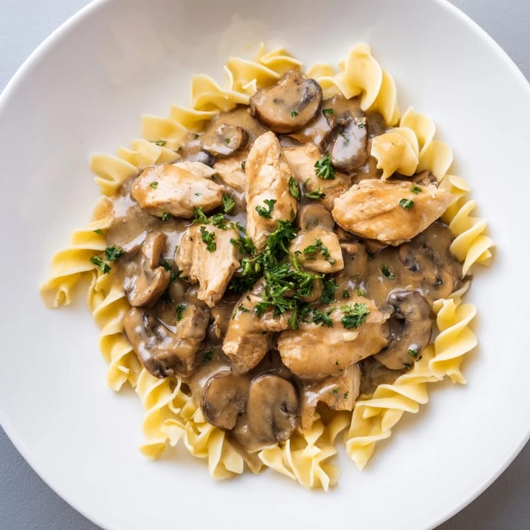 A close-up of creamy chicken stroganoff, showing the velvety sauce and parsley garnish atop.