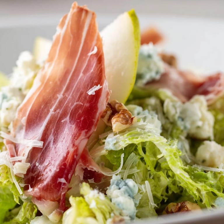 Close-up of Frisée, Pear, Blue Cheese, and Crispy Prosciutto Salad with toasted walnuts and savory shards.