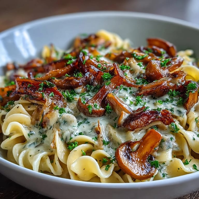 A close-up view of creamy mushroom stroganoff sauce with golden onions over broad egg noodles.